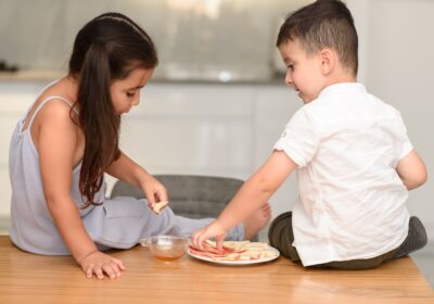 Two children enjoying snacks and dip together, showcasing sibling bonding in a cozy home environment